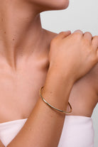 Model wearing the soft gold Louella bangle on her wrist, hand raised to her shoulder.