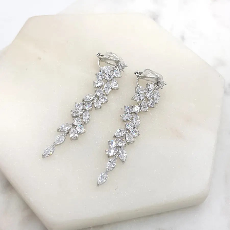 Cubic zirconia leaf-drop clip-on earrings lying flat on marble showing the clip fastening, silver tone