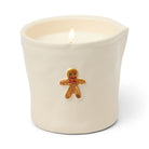 Cream ceramic tumbler candle with a raised gingerbread man in a red bow on the front, lit.