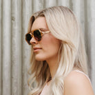 A woman in profile outdoors wearing the Billy sunglasses, showing how they sit on the side of the face