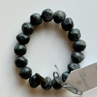 Rock bracelet in Black Marble: a stretch bracelet of chunky black and grey marbled resin beads with its swing tag and metal charm, laid on a pale surface.