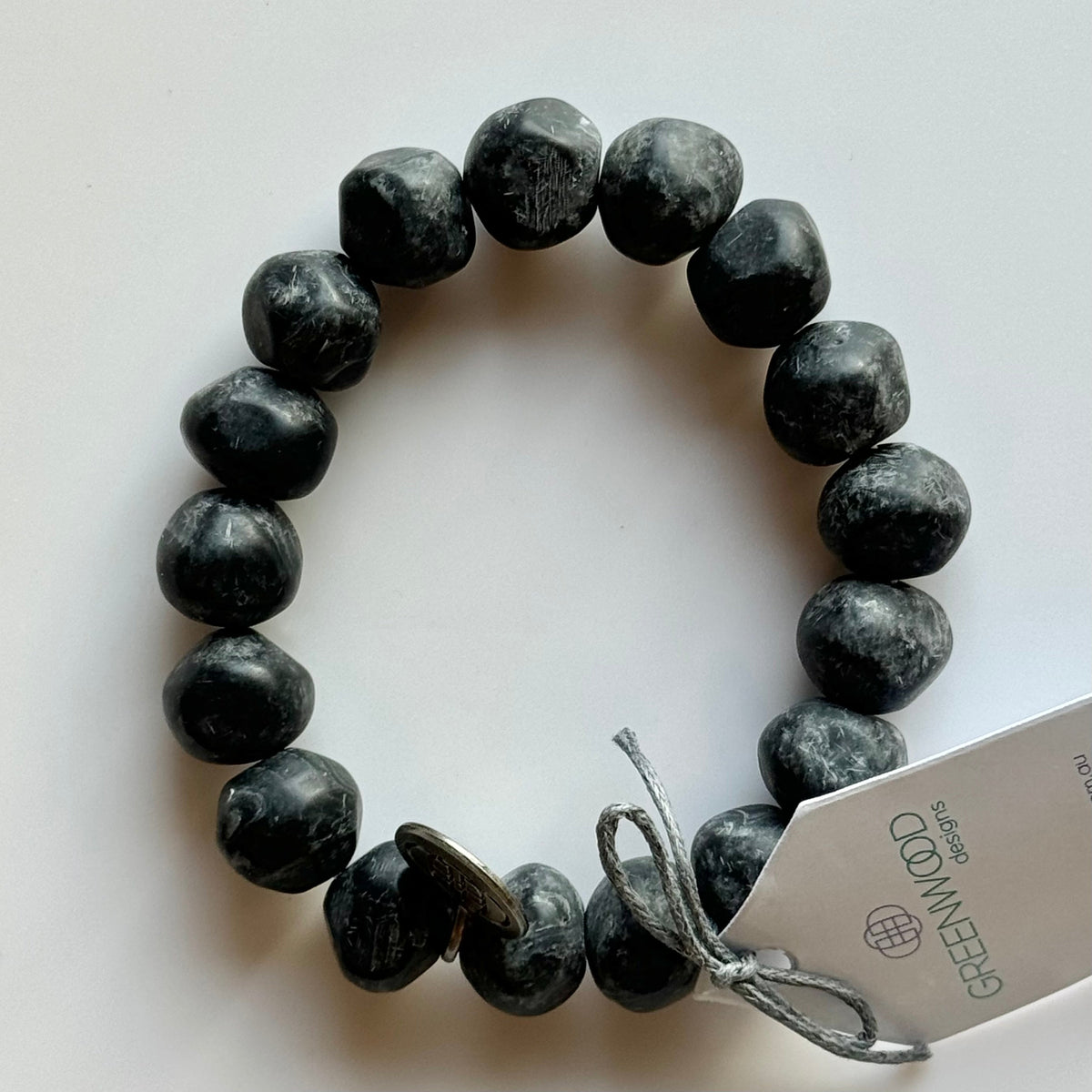 Rock bracelet in Black Marble: a stretch bracelet of chunky black and grey marbled resin beads with its swing tag and metal charm, laid on a pale surface.