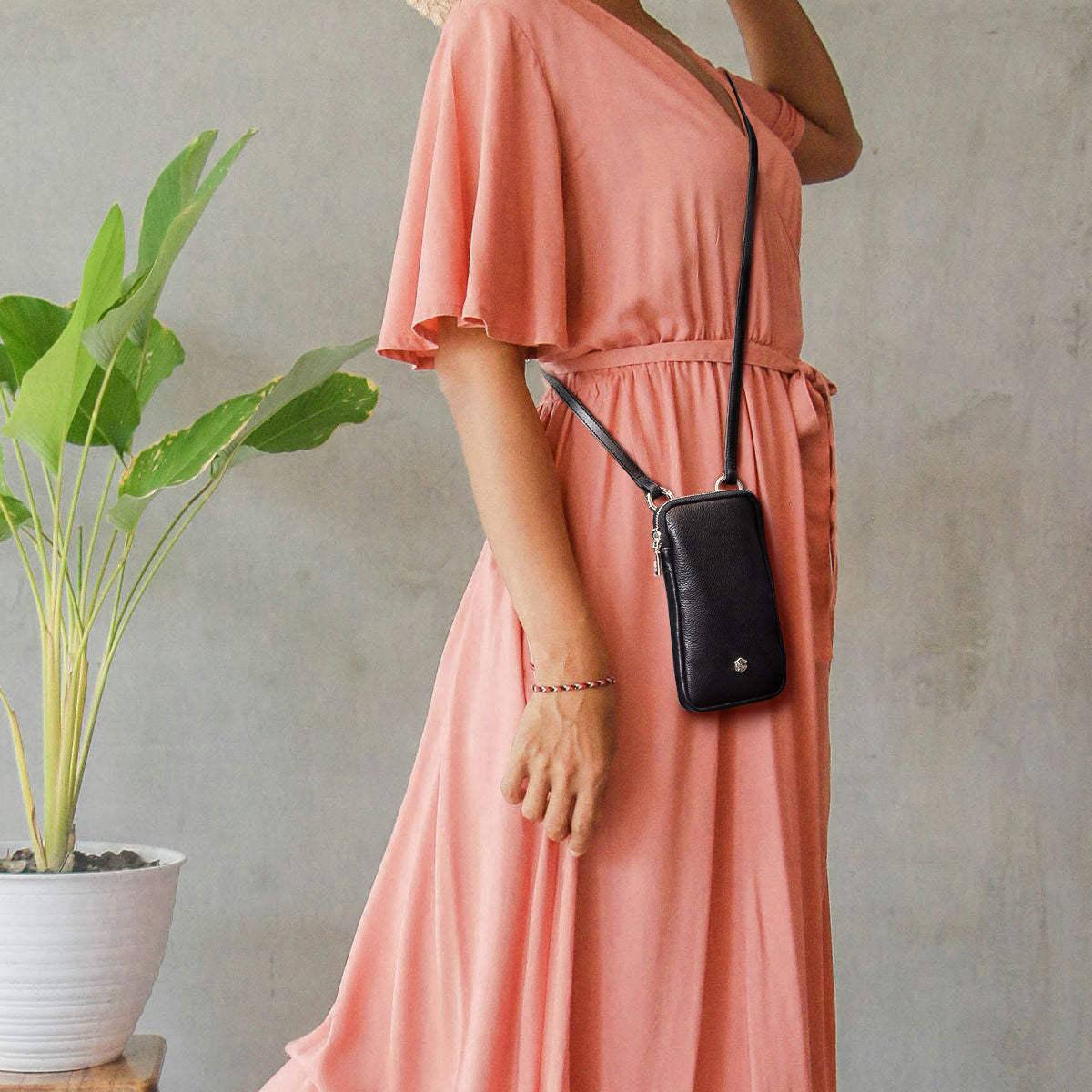 Woman in a coral dress wearing the black leather phone pouch crossbody