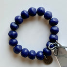 Rock bracelet in Bright Blue: a stretch bracelet of chunky deep cobalt blue resin beads with its swing tag and metal charm, laid on a pale surface.