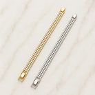 Two three-row cubic zirconia tennis bracelets, one gold tone and one silver tone, lying side by side on marble