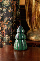 The green and navy striped tree candle on a dark timber side table beside floral curtains and a gilded statue.