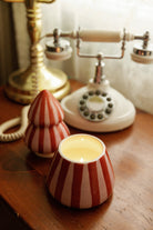 The red and pink striped tree candle lit, its top set aside, on a timber table beside a vintage telephone.