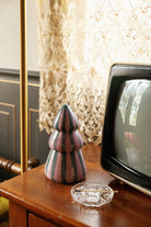 The pink and green striped tree candle on a timber side table beside an old television and a small glass dish.