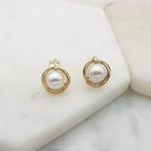 Pair of gold-tone clip-on earrings, each a white freshwater pearl wrapped in an open gold swirl, on marble