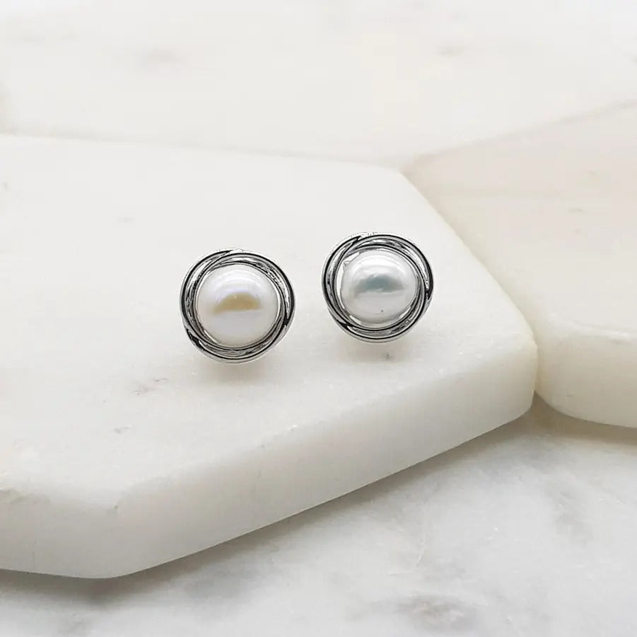Pair of silver-tone clip-on earrings with a white freshwater pearl in an open swirl setting, on marble