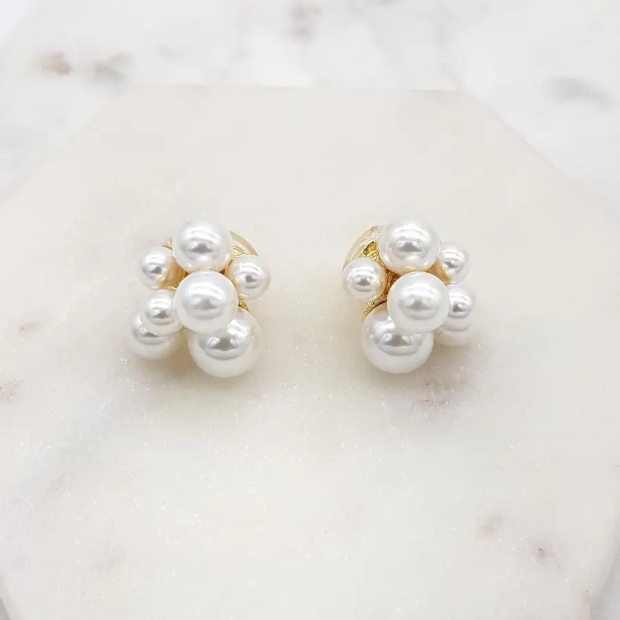 Pair of gold-tone clip-on earrings made of a cluster of white faux pearls in varying sizes, on white marble