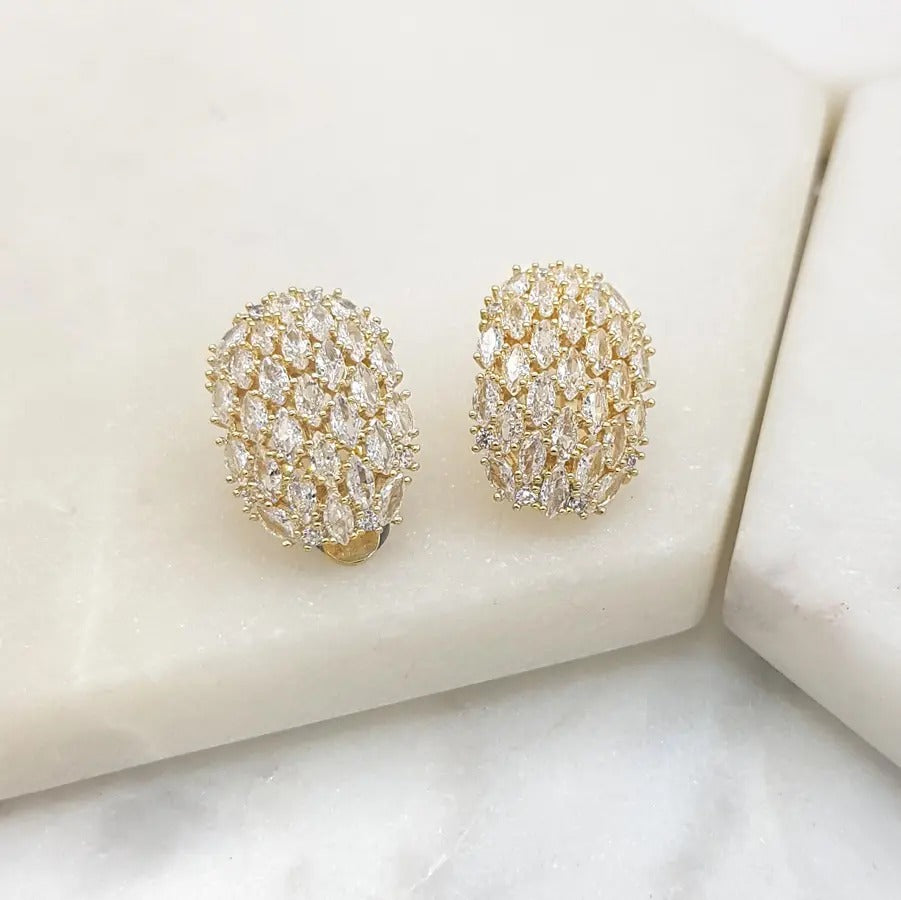 Pair of gold-tone oval clip-on earrings pavé-set with clear cubic zirconia, on white marble
