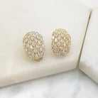 Pair of gold-tone oval clip-on earrings pavé-set with clear cubic zirconia, on white marble