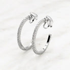 Pair of silver-tone open hoop clip-on earrings lined with clear crystals, on white marble