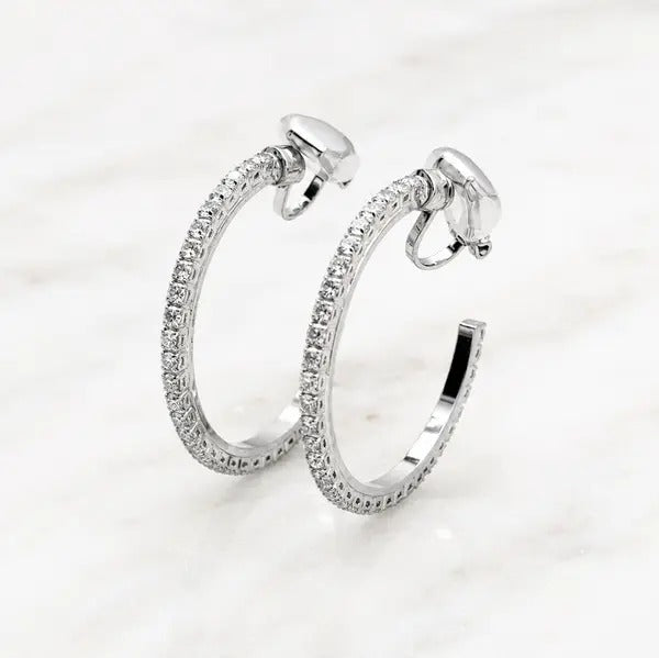 Pair of silver-tone open hoop clip-on earrings lined with clear crystals, on white marble