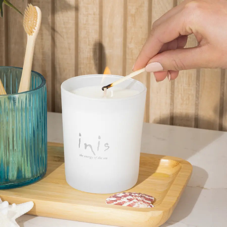 Hand lighting the Inis Scented Candle on a bamboo tray in a bathroom