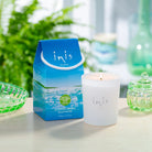 Lit Inis Scented Candle and its gift carton on a table with green glassware