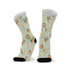 Pair of sage green socks stood side by side, showing the full repeating pattern of hens, chicks and nests wrapping around both socks.
