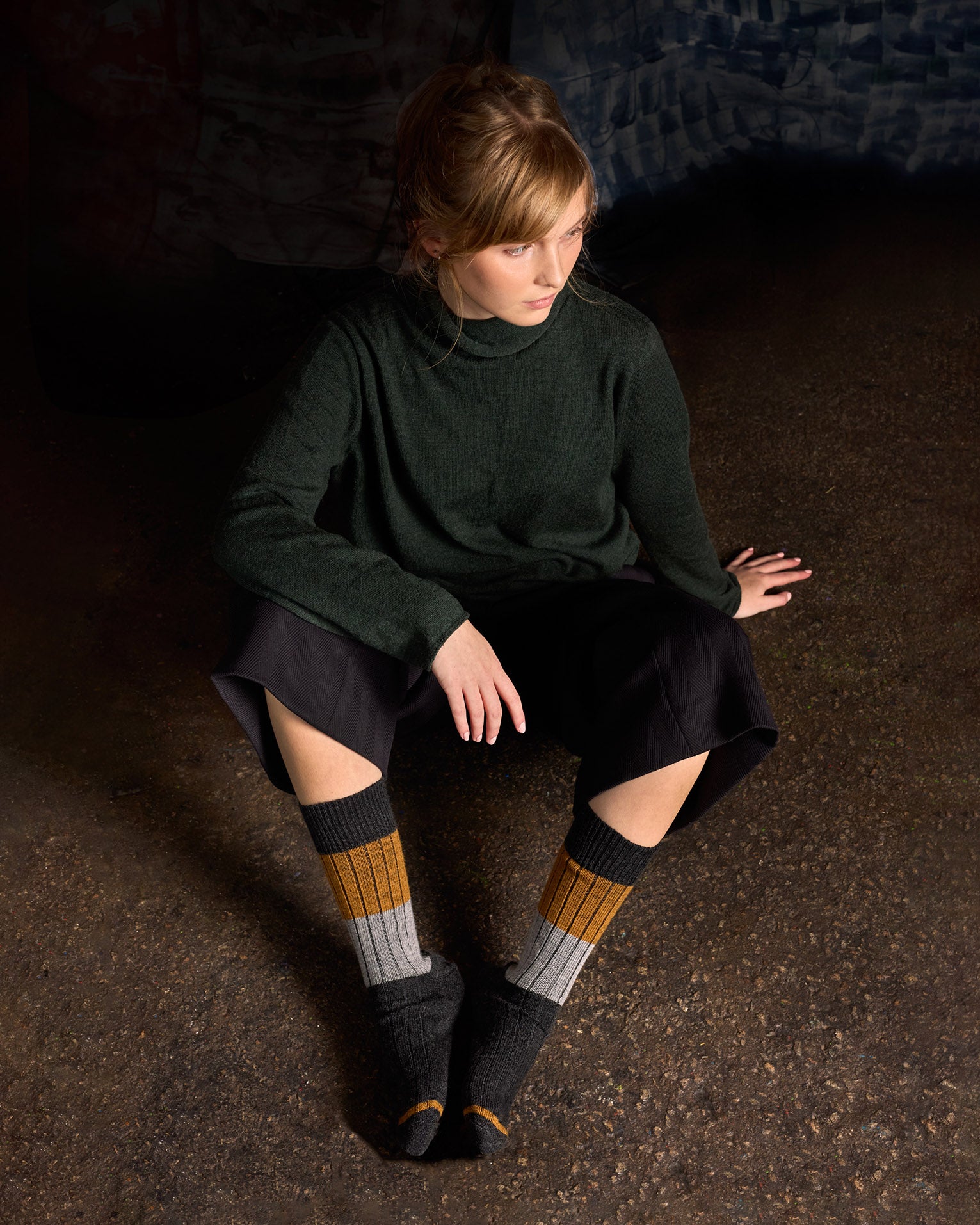 Model seated on the floor in a green knit and shorts, wearing the colour-block rib socks
