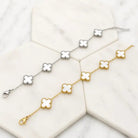 Two five-clover bracelets with white mother-of-pearl clovers, one gold tone and one silver tone, on white marble tiles