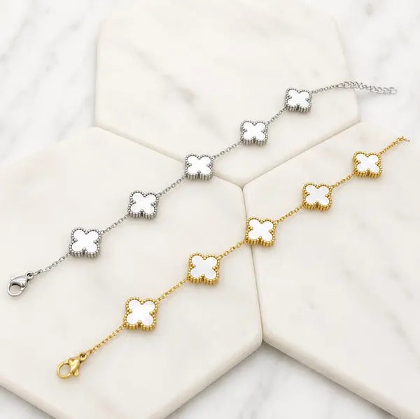 Two five-clover bracelets with white mother-of-pearl clovers, one gold tone and one silver tone, on white marble tiles