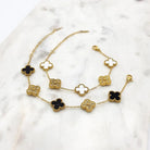 Two gold-tone clover bracelets, one with black clovers and one with white, each alternating with cubic zirconia clovers, on marble