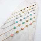Stack of clover bracelets in teal, white, pink and black with cubic zirconia clovers, gold and silver tone, on marble