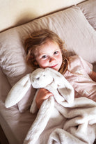 Child in bed holding the ivory bunny lovey blanket