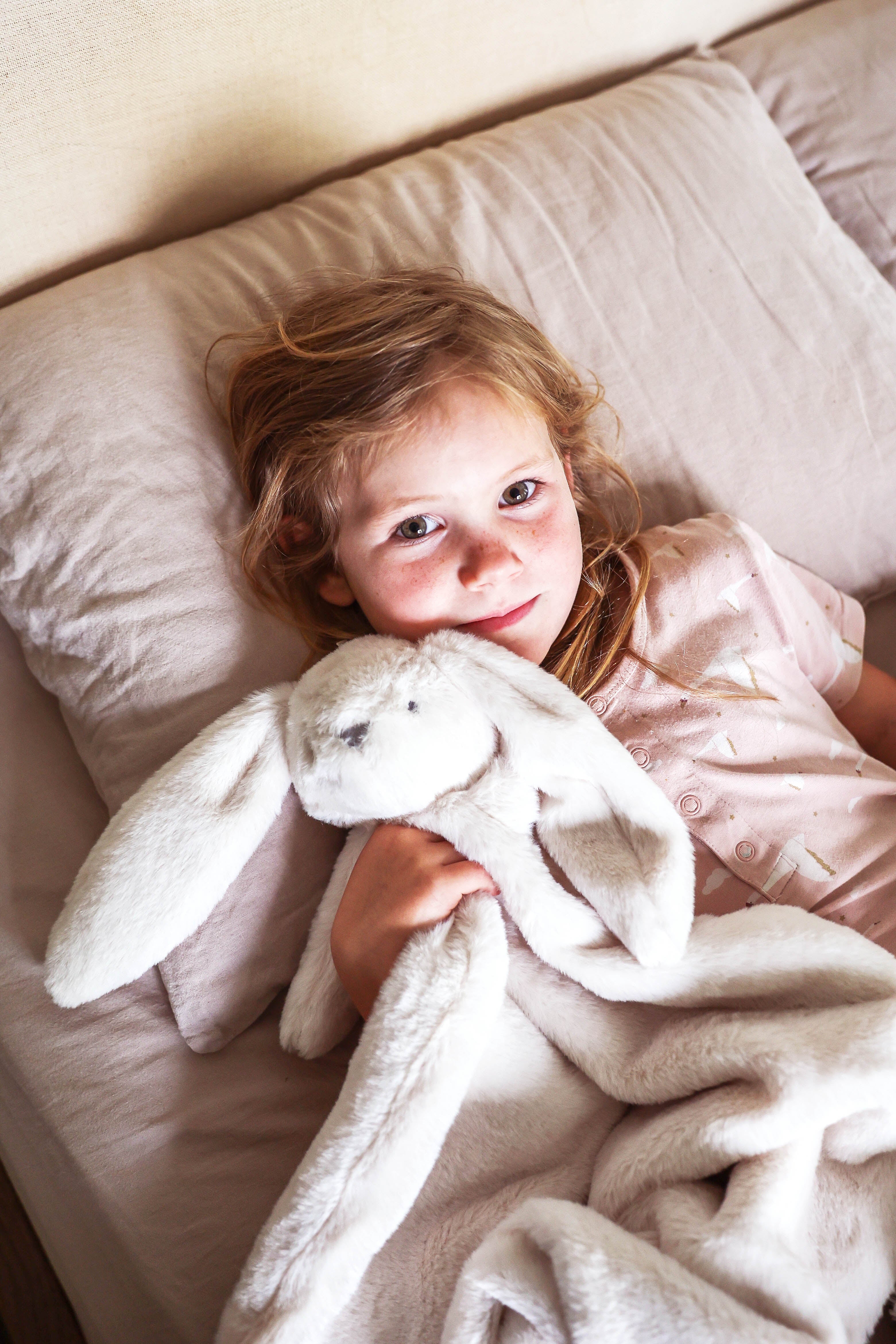 Child in bed holding the ivory bunny lovey blanket