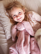 Child in bed cuddling the pink Darcey bunny lovey