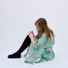 Woman seated on a white floor in a green floral dress and black dotted knee socks