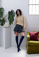 Woman standing by a green velvet chair in a tweed skirt and navy dotted knee socks