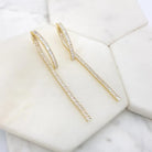 Baguette crystal hoop earrings with a long straight drop, in gold and silver tone, on marble