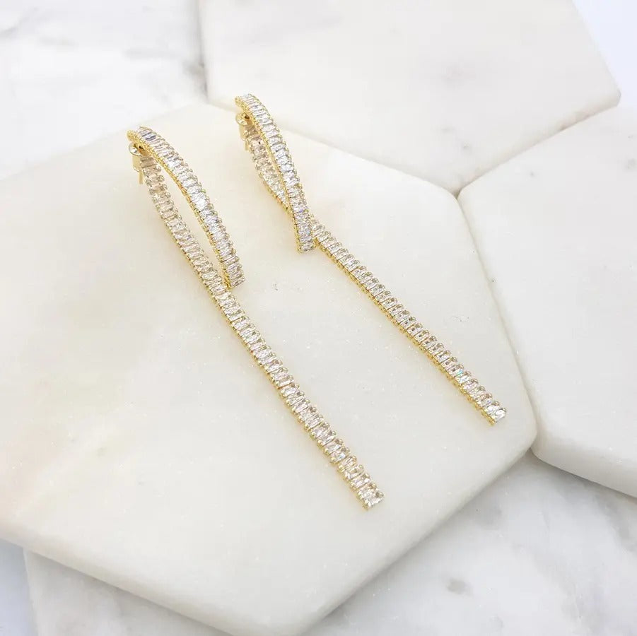 Baguette crystal hoop earrings with a long straight drop, in gold and silver tone, on marble