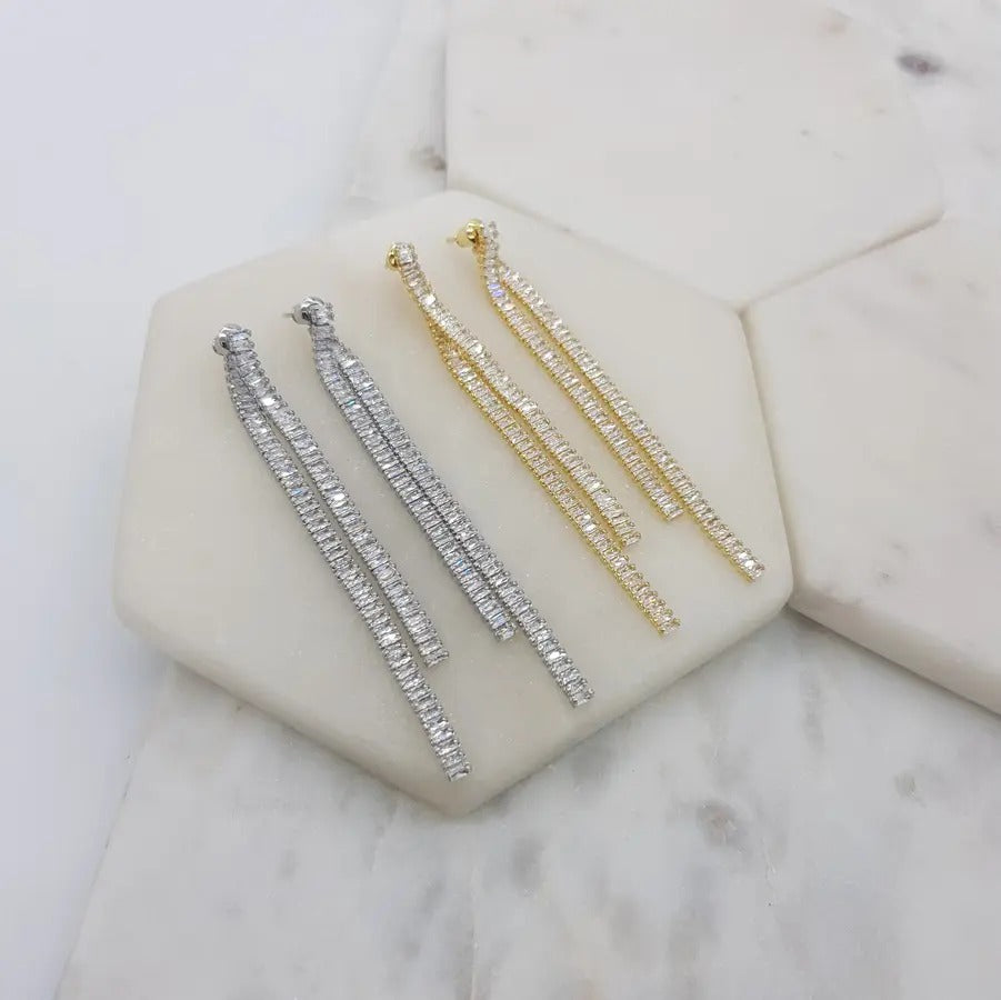 Two pairs of long double baguette drop earrings, silver tone and gold tone, on marble