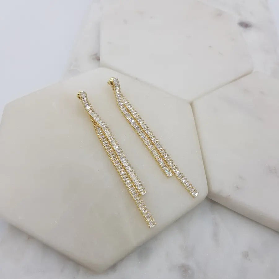 Pair of gold-tone double baguette crystal drop earrings on white marble