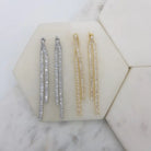 Double baguette drop earrings in silver and gold lying on a marble tile