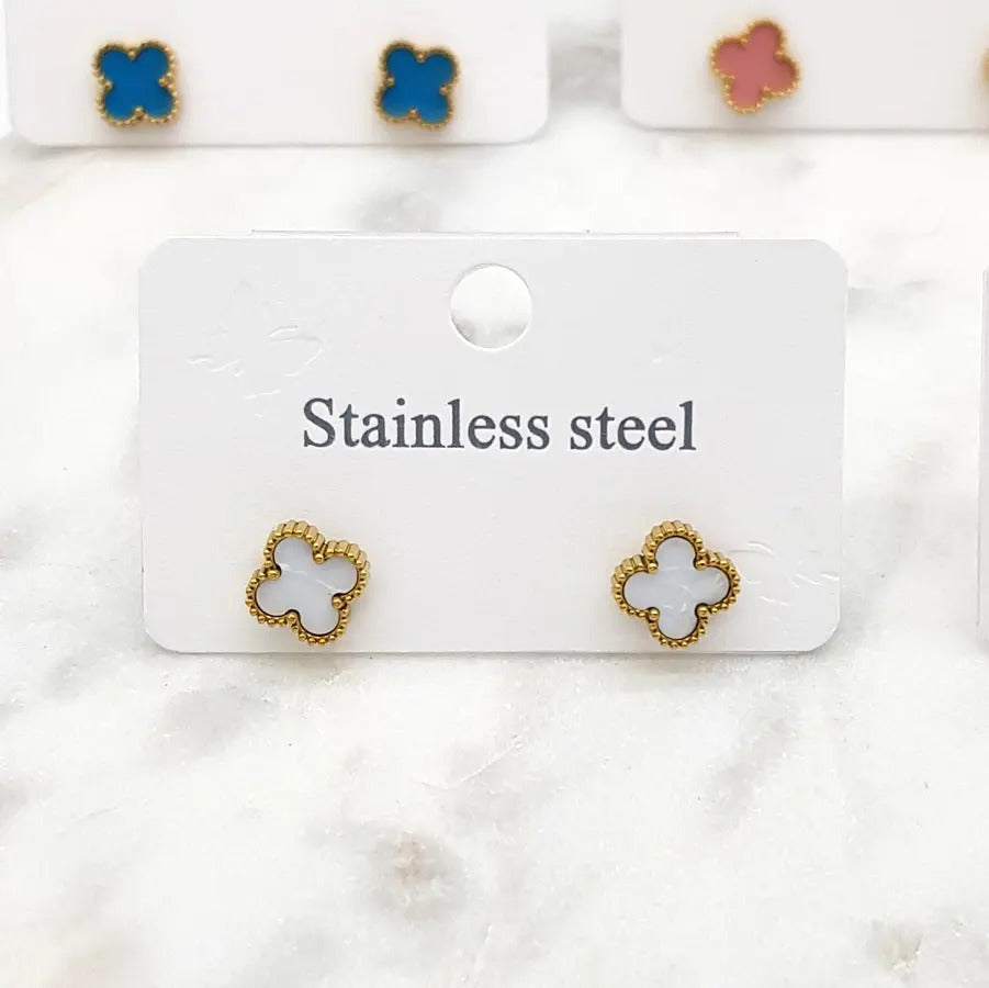 White clover stud earrings on a card, with teal and pink pairs behind, on marble