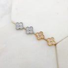 Four pavé cubic zirconia clover studs in a row on marble — two silver-tone in front, two gold-tone behind.