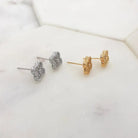 Cubic zirconia clover studs in silver and gold tone lying on a marble tile