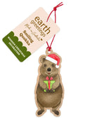 Wooden quokka Christmas decoration hanging from a red twine tie beside its Earth Greetings swing tag - a quokka in a red Santa hat holding a small green wrapped gift.