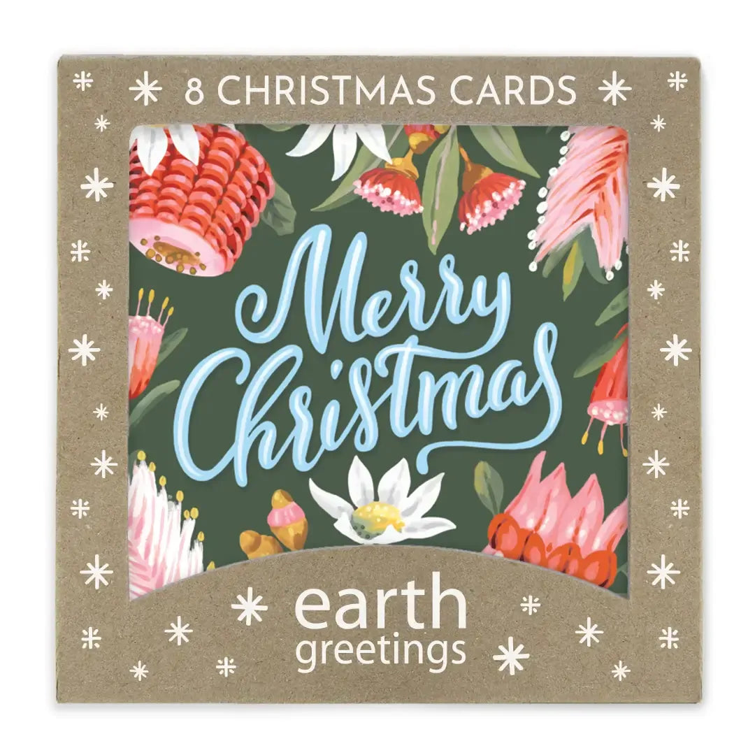 Kraft gift box of eight Christmas cards, its die-cut window showing a deep green card hand-lettered Merry Christmas in pale blue, wreathed in red banksia, pink protea and white flannel flowers.