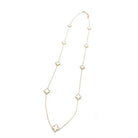 Long gold-tone stainless steel chain necklace set with small white four-leaf clovers spaced along its length, on white