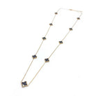 Long gold-tone chain necklace with small black four-leaf clovers spaced along it, on white