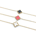 Close-up of three gold-tone clover necklaces with a black, a pink and a white clover on fine chain