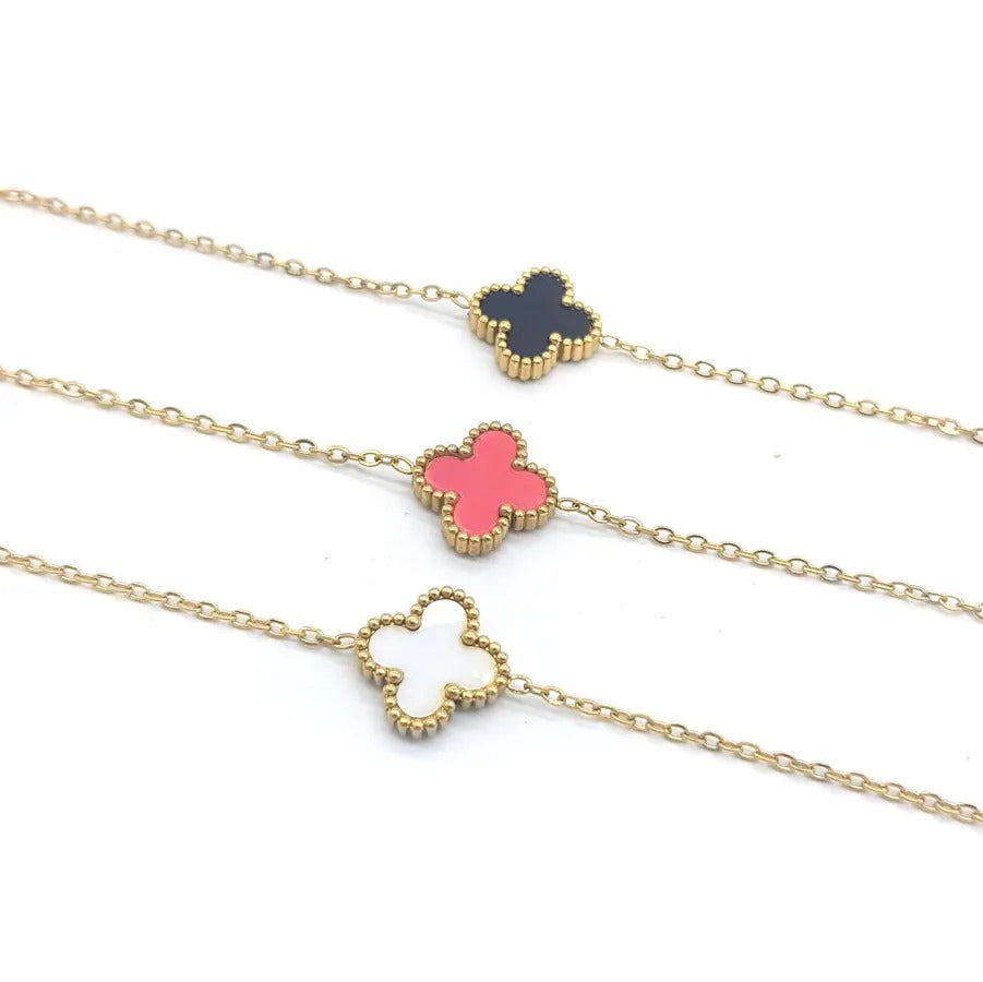 Close-up of three gold-tone clover necklaces with a black, a pink and a white clover on fine chain