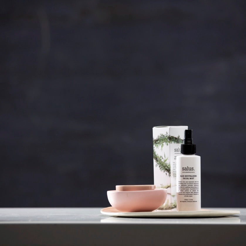 Salus Ultra Moisture Rose Facial Mist bottle on a tray with pink ceramic bowls against a dark wall