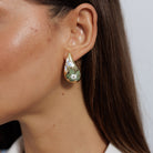 Close view of the gold teardrop dome earring with a painted white and green flower.