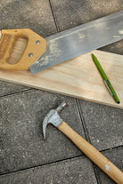 Olive green tooling pen on a timber offcut beside a hand saw and a claw hammer