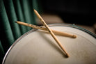 The two drumstick pens resting crossed on a drum skin against a dark green backdrop